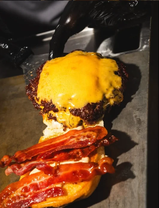 Smash burger con cheddar appena sollevato dalla piastra sopra il bacon croccante