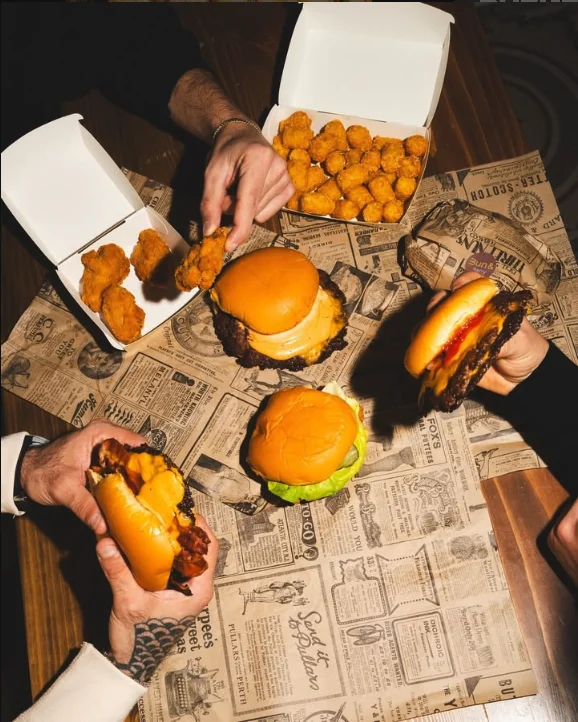Burger, nuggets e potato pops su un tavolo coperto di carta di giornale, visti dall'alto